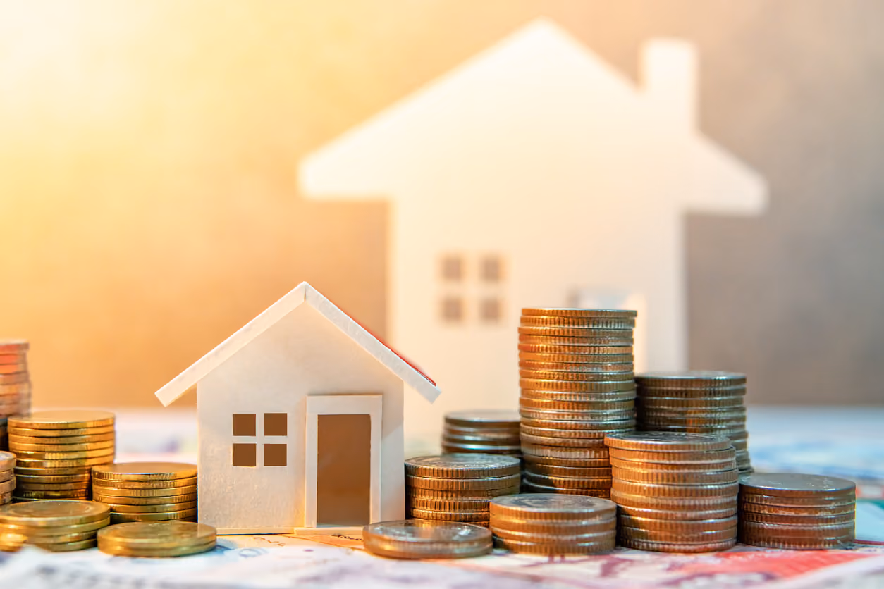 A miniature model of a house surrounded by stacks of quarters illustrating the financial aspect of buying a home.