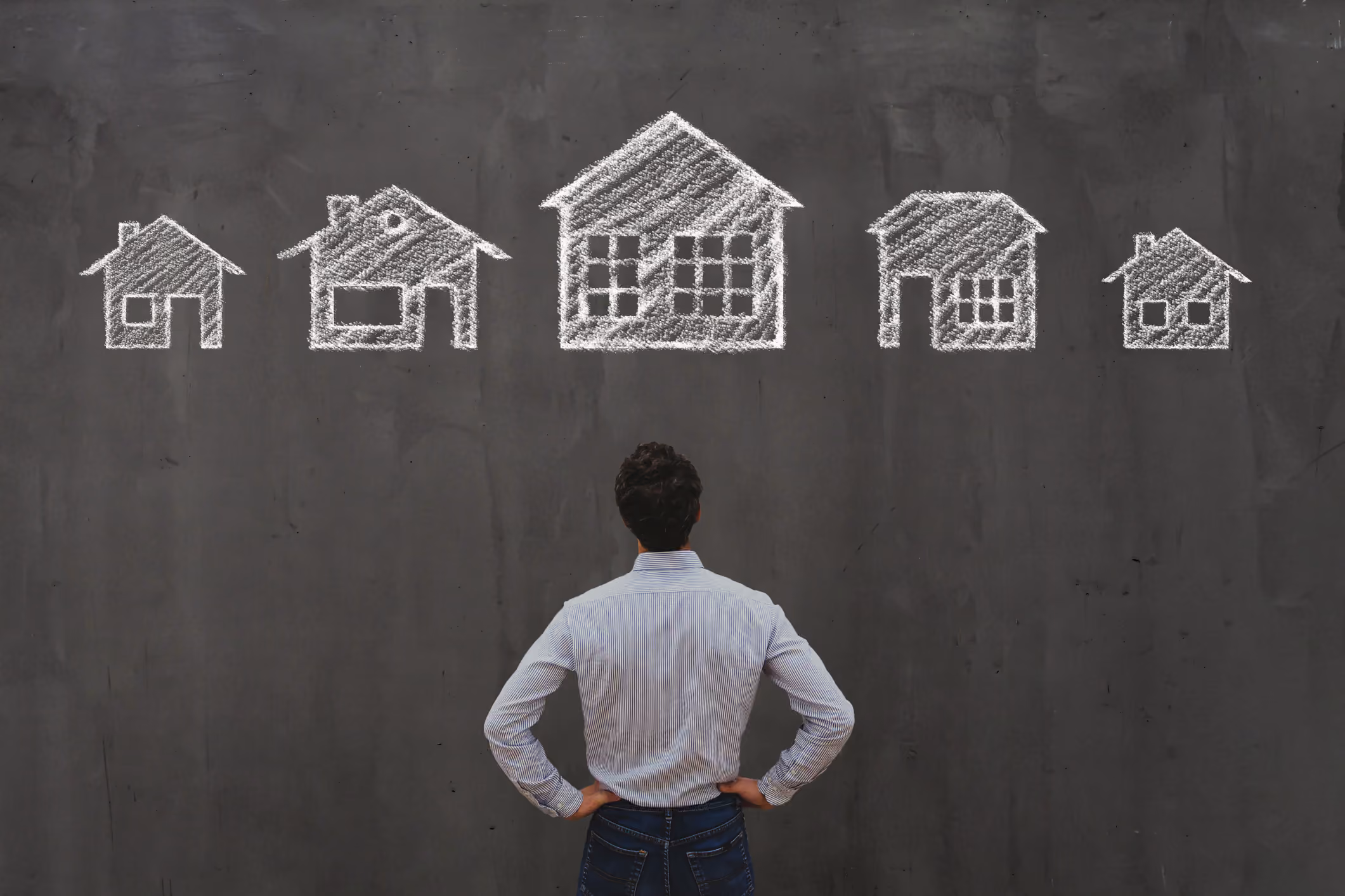 Person facing a chalkboard with drawings of houses in different sizes.