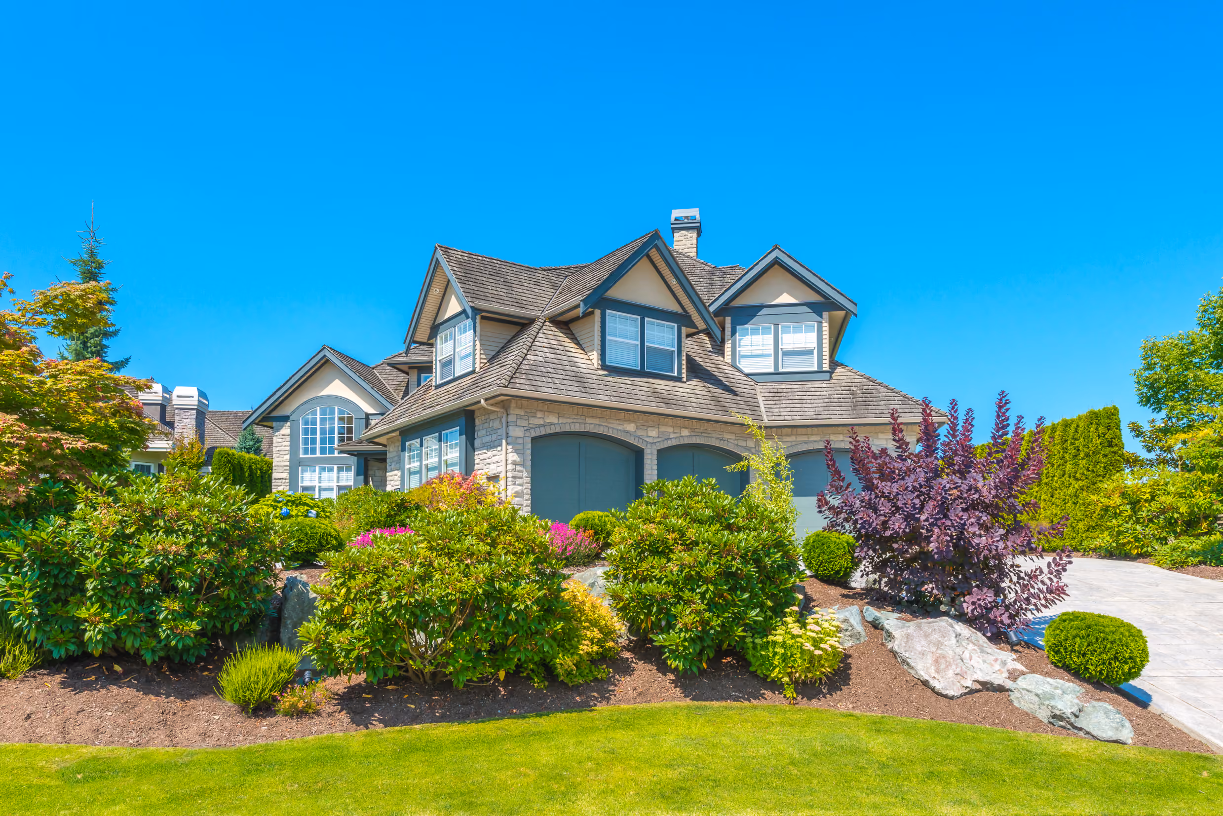 Image of a beautiful large home, with a large, lush, green garden covering the lawn.